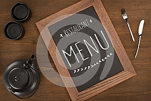 top view of restaurant menu in wooden frame, tea set and cutlery