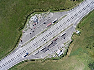 Top view at resting area of tollway with parked freight long vehicles and passenger cars, a cafe and toilets