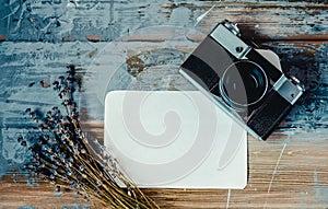 Top view of a retro camera, lavender bouquet and paper on the brown wooden textured background