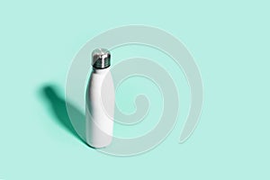 Top view of reusable steel eco thermo water bottle of white, with shadow, on background of aqua menthe color.