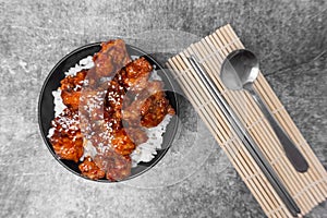 Top view Rice topped Korean spicy deep-fried chicken topped white sesame on the gray concrete table, popular street food in Korea