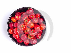 Top view of ripe red acerola cherries fruit in a ceramic bowl isolated on white background.
