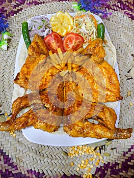 Top view of roast chicken with raw chopped onion and vegetables on a plate on a woven surface