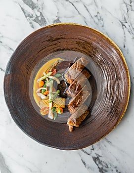 Top view of roasted medium rare wagyu beef served with sour sauce with roasted baby vegetables on stone plate