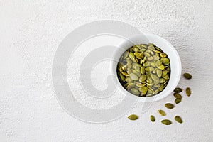 Top view of roasted pumpkin seeds in white bowl. Dry Pepita after shelling on white background. Copy space