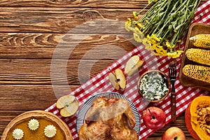Top view of roasted turkey, pumpkin pie and grilled vegetables served on wooden table with flowers and plaid napkin.