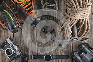 Top view of rock climbing equipment on wooden background. Chalk bag, rope, climbing shoes, belay/rappel device, carabiner and asce