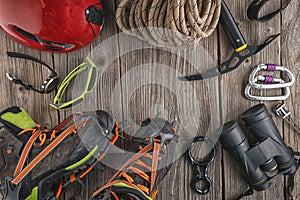Top view of rock climbing equipment on wooden background. Chalk bag, rope, climbing shoes, belay/rappel device, carabiner and asce