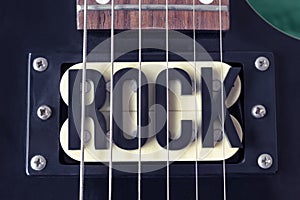 Top View of a ROCK lettering black word in middle of a six black electric guitar strings and yellow microphones