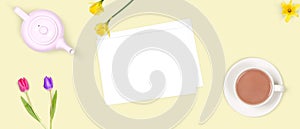 Top view of a romantic scene of a cup of tea, a tea pot, flowers and an envelop. Background, banner or scene related to easter,