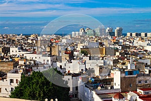 Top view of the rooftops of Casablanca with lots of satellite dishes and drying clothes. In the distance high-rise buildings,