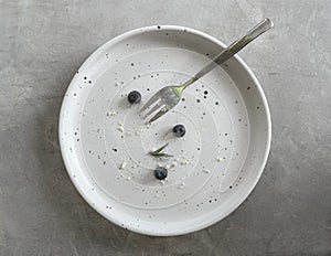 Top view of round white ceramic plate with fork, Dirty dishe after eating blueberry cheese tart is finished.