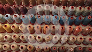 Top view of rows of spools of thread for sewing in different colors and shades on a rack in a production workshop or