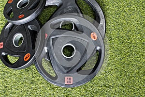 Top view of rubberized barbell plates on the artificial grass mat of a home gym. Various weights labeled in kilograms