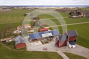 Top view of rural landscape on sunny spring day. Farm with solar photo voltaic panels system on wooden building, barn or house