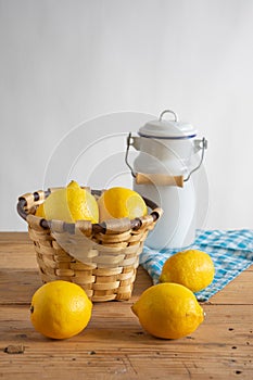 Top view of rustic table with basket with lemons, cloth and milk jug, white background, vertical