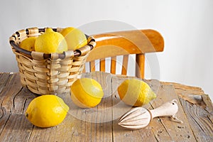 Top view of rustic table with basket with lemons and wooden juicer, white background with chair,