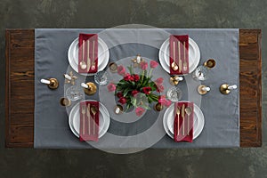 top view of rustic table setting with red tulips bouquet, tarnished cutlery, wine glasses, candles and empty plates on tabletop