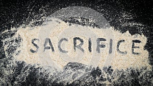 Top view of SACRIFICE word written on white sand