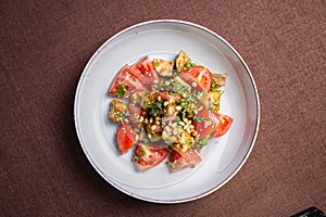 Top view salad of fresh tomatoes and avocado with pine nuts and herbs on a white plate