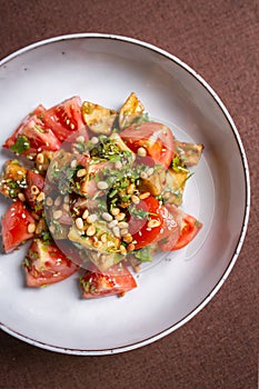 Top view salad of fresh tomatoes and avocado with pine nuts and herbs on a white plate