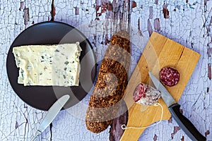 Top view of salami cut on wooden table with bread with cereals and fresh cheese