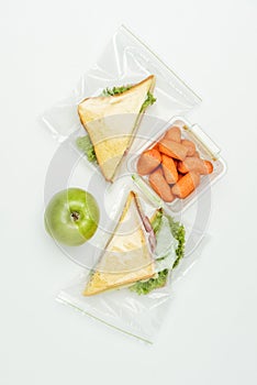 top view of sandwiches in ziplock bags and carrots in lunch box on white
