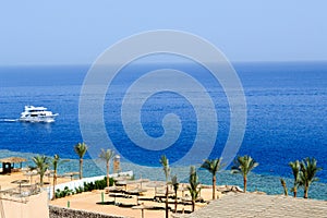 Top view of a sandy beach with sunbeds and sun umbrellas and two large white ships, a boat, a cruise liner floating in the sea on