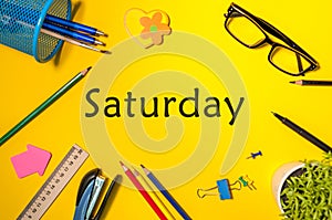 Top View of Saturday - word on yellow workplace with office or school supplies. Time Management and Schedule Concept