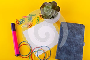 Top view on school, office stationary on yellow background. Bright pen, notebook, colorful paperclips, blank paper sheet for your