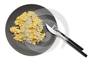 Top view of scrambled eggs with fresh green chives on dark grey plate with elegant cutlery isolated on white background