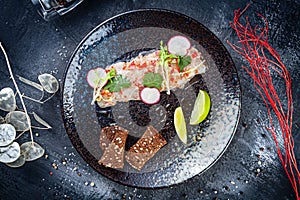 Top view on sea bass ceviche served in dark plate on black stone background. Top view food. Flat lay seafood. Fresh and tasty