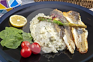 Top view of Sea bass fillet steak with vegetable in black round plate