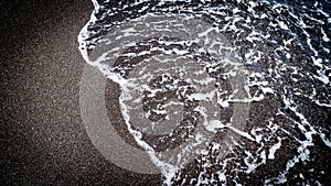 Top view of seawater splashing on a sandy beach in Santorini, Greece