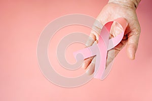 Top view of senior woman hand supports Breast Cancer Day by holding Pink Ribbon Breast Cancer Awareness with copy space