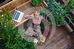 Top view of senior woman with laptop sitting outdoors on terrace, resting.