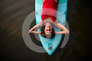 Top view of senior woman lying on paddleboard on lake in summer, resting.