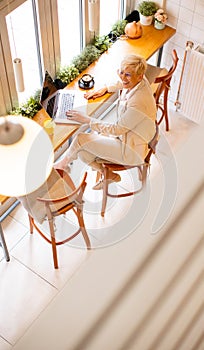 Senior woman using mobile phone while working on laptop and drinking fresh orange juice in the cafe