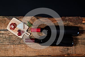 Top view of served snacks on board with twig of rosemary and bottles of red wine on wood