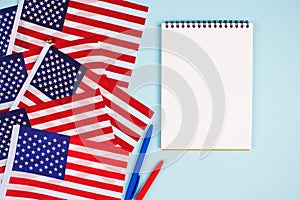 Top view on set of american flags, red and blue pens and empty notebook with copyspace for text on light blue background. National