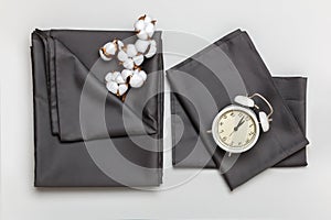 Top view of a set of gray bed sheets, pillow cases, duvet cover, cotton branch and alarm clock