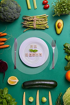 Top view set of healthy vegetables, white plate with Go vegan message on wooden blocks on green background. Vegetarian and vegan