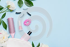Top view of set of make up and skin care products spilling out of cosmetics bag on blue background with white flowers and copy