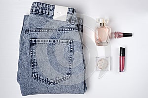 Top view of set of woman clothes and beauty accessories on the whie surface.Blue jeans, bottle of perfume, blish, nail polish and