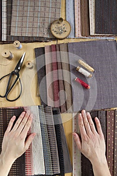 Top view of sewing table with fabrics, supplies for home decor or quilting project and woman`s hand