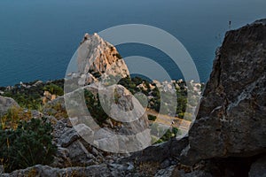 top view of sharp rocks cliff among green trees on the shore, coast of blue sea, Crimea, summer, sunset