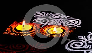 Top view of shining designed terracotta lamps with white and red rangoli art on black background. diwali concept