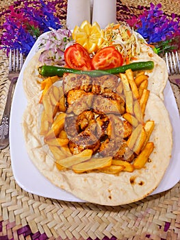 Top view of Shish taouk and fries on a flatbread with onion and vegetables