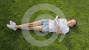 Top view shot of beautiful teenage girl lying on grass and reading a book