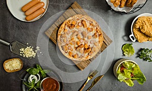 Top view shot of delicious tasty juicy sliced sausage cheesy pizza placed on wooden board around with other fast food crispy fried